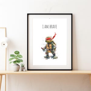 May include: A black framed print with a white background featuring a cartoon illustration of a Teenage Mutant Ninja Turtle with a red bandana and the text "I AM BRAVE".