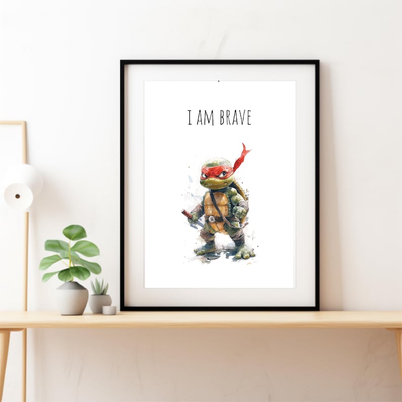 May include: A black framed print with a white background featuring a cartoon illustration of a Teenage Mutant Ninja Turtle with a red bandana and the text "I AM BRAVE".