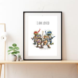 May include: A white framed print with a watercolor illustration of four Teenage Mutant Ninja Turtles. The turtles are standing in a row, facing forward. The text "I AM LOVED" is printed in black at the top of the print.