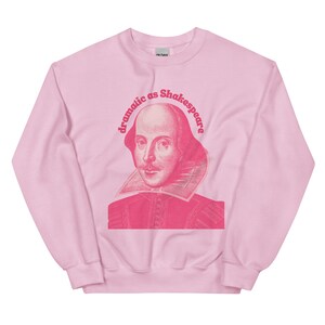 May include: Pink sweatshirt featuring a pink image of William Shakespeare and the text "dramatic as Shakespeare" in a retro font.