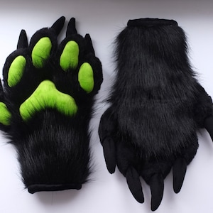Peut inclure: Une paire de mitaines en fourrure noire avec des coussinets de pattes verts. Les mitaines ont des griffes sur les doigts.