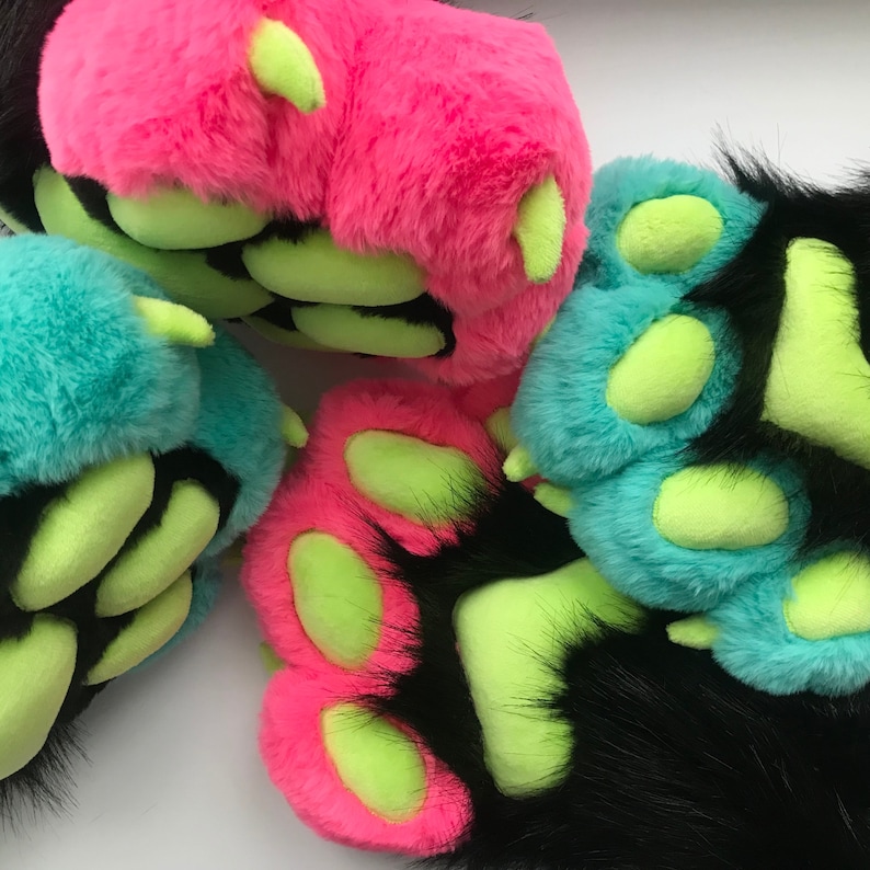 May include: Close-up of colorful furry paw pads in bright pink, teal, and black, with neon green toe pads. The plush paws have long black fur around the edges.