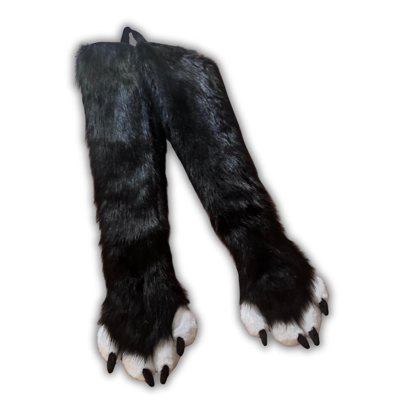 May include: A pair of black faux fur leg warmers with large paw-like feet. The feet have white pads and black claws. The leg warmers are connected at the top with a black loop.