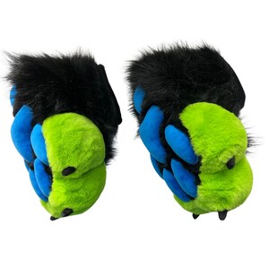 May include: A pair of furry paw-shaped slippers. The slippers have black fur on top, with blue and lime green claws. The claws are made of a soft, plush material. The slippers are designed to resemble animal paws.