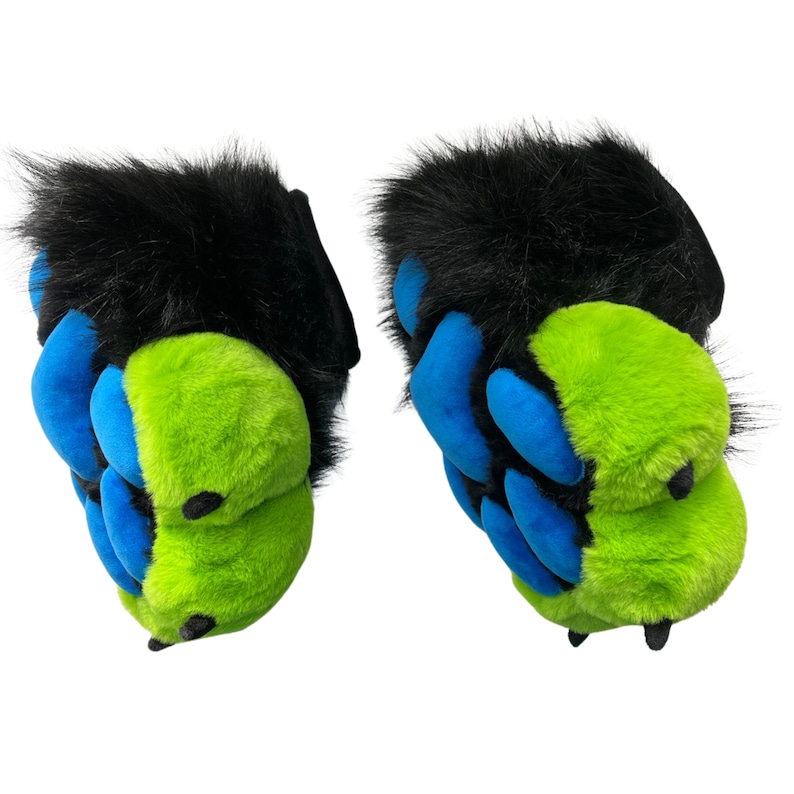 May include: A pair of furry paw-shaped slippers. The slippers have black fur on top, with blue and lime green claws. The claws are made of a soft, plush material. The slippers are designed to resemble animal paws.
