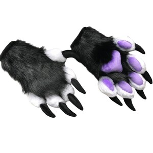 May include: A pair of furry paw gloves in black, white, and purple. The gloves have long black claws and are designed to resemble animal paws. The fur is black and white, with purple pads on the palms and fingers.
