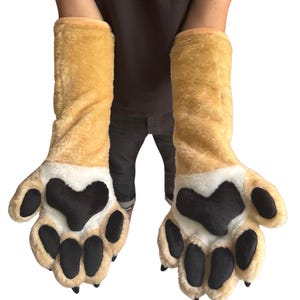 May include: A pair of plush, oversized paw gloves. The gloves are tan with white accents and large black paw pads. The gloves extend up the arm and are designed to resemble animal paws.