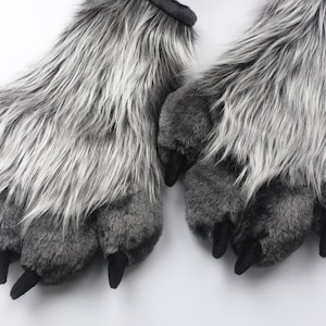 Peut inclure: Une paire de marionnettes de main en forme de patte de loup en fourrure grise et blanche avec des griffes noires.