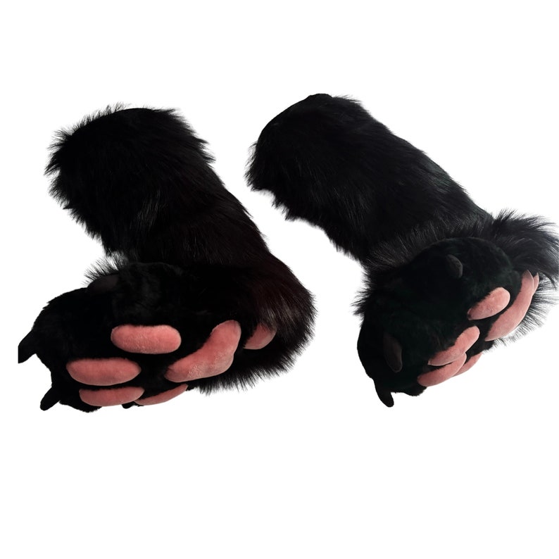 May include: A pair of black faux fur bear paws with pink paw pads. The paws are detailed with individual toe shapes and claws. The fur is long and fluffy, giving a realistic appearance. The paws are designed to be worn as part of a costume.
