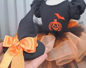 May include: A black and orange Halloween costume for a child. The costume includes a black witch hat with an orange bow, and a black dress with orange and black tulle skirt. The dress has a pumpkin and bat design.