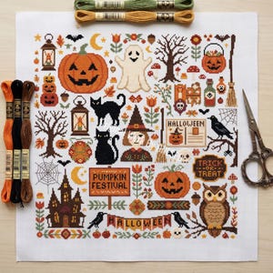 May include: A white fabric square featuring a colorful Halloween-themed cross-stitch pattern with pumpkins, a ghost, a witch, a black cat, an owl, a haunted house, and text reading Pumpkin Festival and Trick or Treat, accompanied by embroidery floss and scissors.