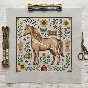 May include: A cross-stitch design featuring a tan horse in a field of sunflowers, stars, and wheat. The design is framed with a brown border and includes the text "Original Work By ONESEG". Embroidery floss and scissors are also in the image.