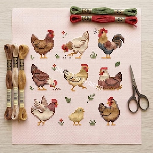 May include: A cross-stitch project featuring various chickens and a rooster in shades of brown, red, and yellow. Embroidery floss in green, red, and brown, along with scissors, are also visible. The design is on a pink canvas.