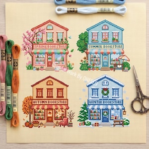 Könnte beinhalten: Ein Kreuzstichmuster auf beigem Stoff mit vier saisonalen Buchhandlungen, beschriftet als Spring, Summer, Autumn und Winter. Das Design zeigt farbenfrohe Fassaden, Bäume und saisonale Dekorationen. Drei Stickgarnstränge und eine Metallschere.