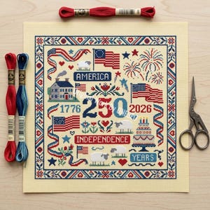 May include: A patriotic cross-stitch design featuring American flags, fireworks, and the text "America" and "Independence." The design includes the numbers "1776" and "2026," with "250" in the center. Red, white, and blue embroidery floss and scissors are included.