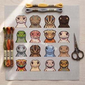May include: A cross-stitch pattern on light gray Aida fabric featuring a grid of sixteen distinct lizard portraits in various colors and patterns. The kit includes three skeins of green, orange, and brown embroidery floss, two yellow and gray skeins, and a pair of ornate metal scissors.