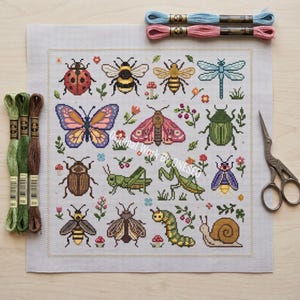 May include: A square cross-stitch fabric panel featuring a grid of colorful insects including a ladybug, bees, a dragonfly, a butterfly, a moth, a beetle, a grasshopper, a praying mantis, a caterpillar, and a snail, with embroidery floss and scissors.