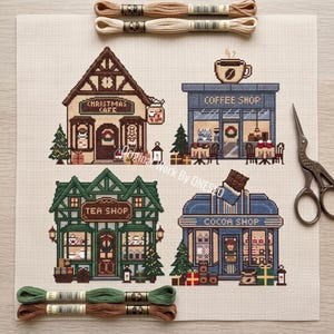 May include: A cross-stitch pattern on cream fabric featuring four storefronts: a brown Christmas Cafe, a blue Coffee Shop, a green Tea Shop, and a blue Cocoa Shop. The design includes holiday decorations, trees, and gifts. Two sets of embroidery floss are included.
