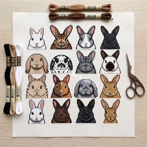 May include: A cross-stitch pattern on white Aida fabric featuring a grid of sixteen different rabbit portraits in various colors and breeds. The kit includes three skeins of embroidery floss on the left, two on the top, and metal scissors.