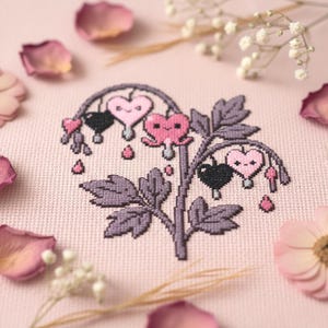 Puede incluir: Punto de cruz de una flor de corazón sangrante en tonos rosa, negro y gris. El diseño presenta flores en forma de corazón con caras sonrientes y detalles de lágrimas, sobre un fondo de tela rosa claro. Pétalos y ramitas de flores secas rodean el punto de cruz.