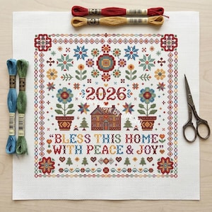 May include: A white cross-stitch fabric featuring a colorful pattern with the year 2026, a house, flowers, and the text BLESS THIS HOME WITH PEACE & JOY, accompanied by four skeins of embroidery thread in red, yellow, blue, and green, and metal scissors.