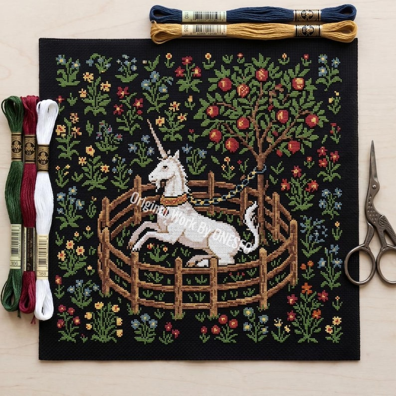 May include: A black needlepoint canvas featuring a white unicorn within a wooden fence, chained to a tree laden with red apples. The scene is surrounded by colorful flowers. Embroidery floss in green, red, white, yellow, and blue, and a pair of scissors are also visible.