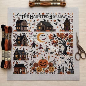 May include: A cross stitch pattern titled The Haunted Hollow featuring various houses, pumpkins, ghosts, bats, and a large tree on light fabric. The set includes three skeins of embroidery floss on the left, two on top, and vintage-style scissors on the right.