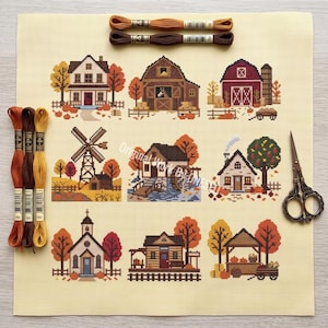 May include: A cross stitch fabric piece featuring nine distinct autumn-themed scenes including houses, a barn, a windmill, and a church. The kit includes three skeins of brown and orange embroidery floss at the top, three on the left, and scissors.