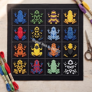 May include: A black fabric square featuring a cross-stitch grid of sixteen colorful frogs in various patterns and hues, including blue, green, yellow, red, and orange. The text Original Work By ONESEO is printed across the center of the grid.