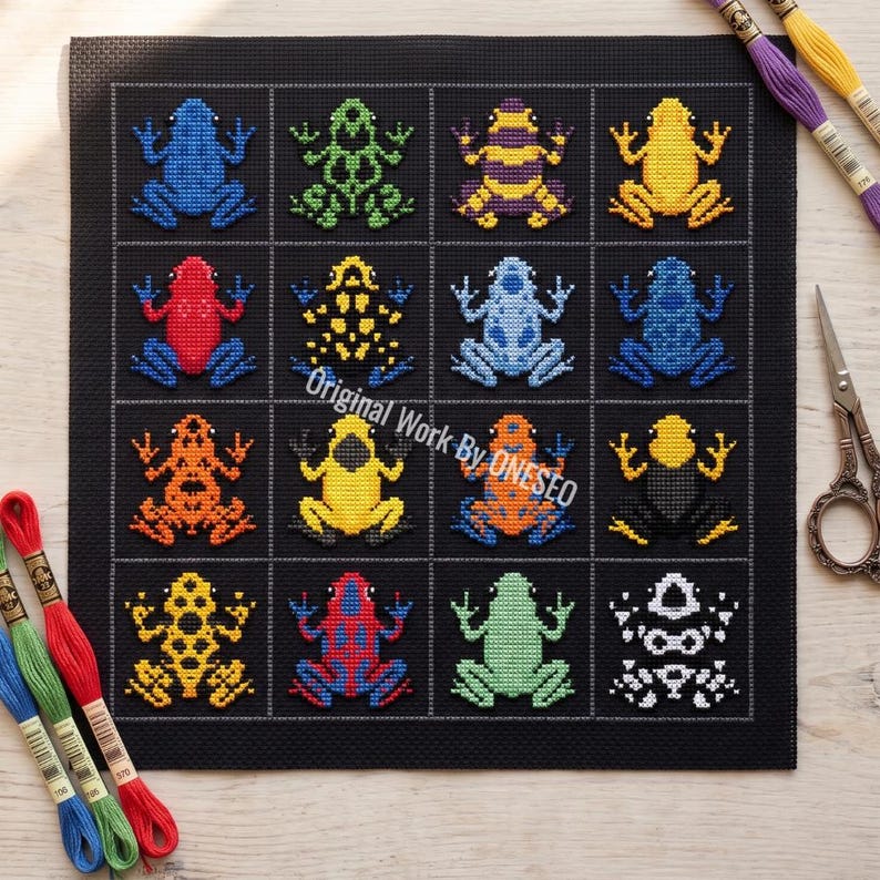 May include: A black fabric square featuring a cross-stitch grid of sixteen colorful frogs in various patterns and hues, including blue, green, yellow, red, and orange. The text Original Work By ONESEO is printed across the center of the grid.