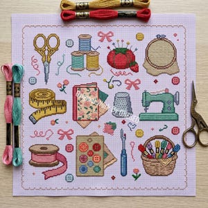 May include: A light purple cross-stitch fabric featuring various sewing motifs including scissors, spools of thread, a pincushion, a measuring tape, a sewing machine, buttons, and a basket of embroidery floss, with two loose skeins of thread and metal scissors.