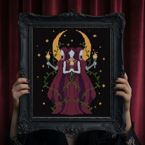 May include: Black framed cross-stitch art featuring three figures in burgundy robes, holding torches, beneath a crescent moon. Green vines and gold stars decorate the black background. The frame has ornate detailing.