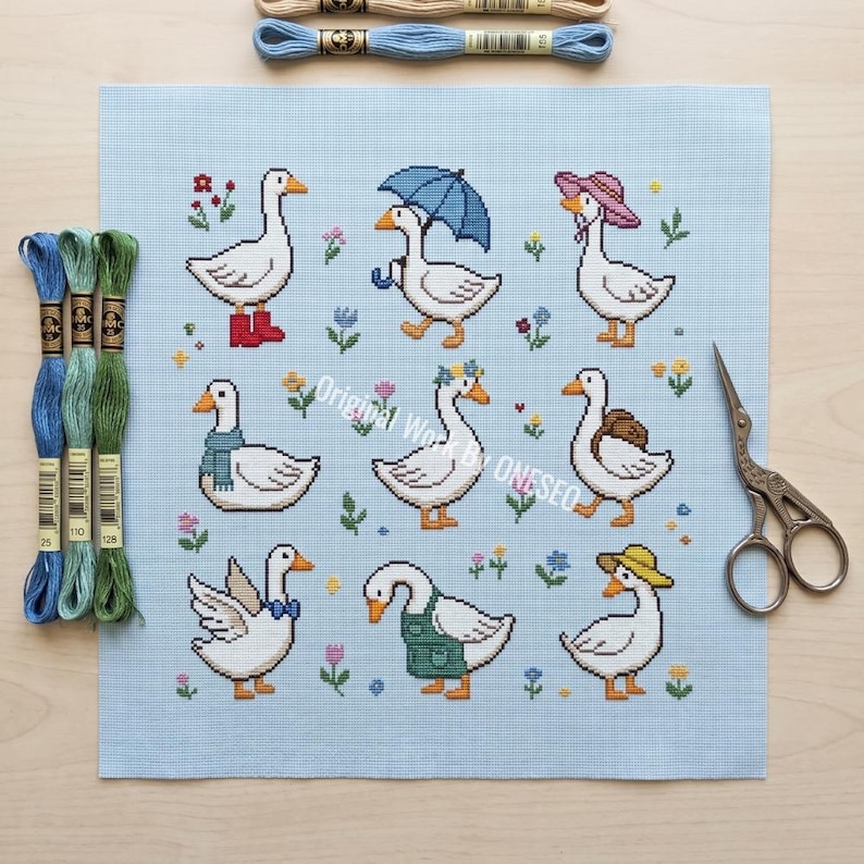 May include: A cross-stitch pattern featuring nine geese, each adorned with unique accessories like boots, hats, and scarves. The geese are set against a light blue background with floral accents. Embroidery floss and scissors are also visible.