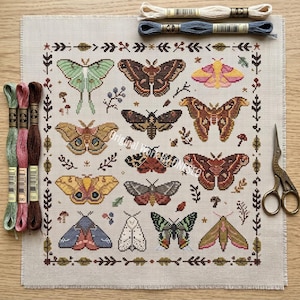Pode incluir: Um padrão de ponto cruz em tecido bege apresentando doze mariposas distintas em várias cores, incluindo verde, castanho, rosa e amarelo, rodeadas por uma borda botânica, com três meadas de fio de bordar e tesouras de estilo vintage.