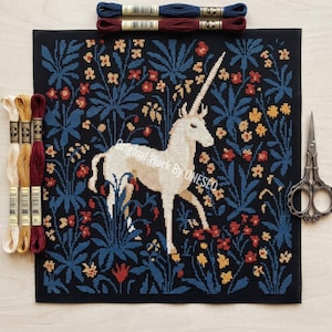 May include: A cross-stitch canvas depicting a white unicorn amidst a floral pattern with blue, red, and yellow details. Embroidery threads in various colours and a pair of scissors are placed around the canvas. The text "Original Work By ONESEQ" is visible.