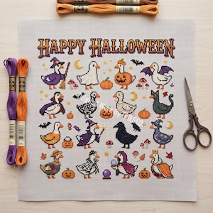 May include: A cross-stitch pattern on white fabric featuring the text HAPPY HALLOWEEN and various geese in costumes, including a witch, vampire, and ghost, surrounded by pumpkins, bats, and mushrooms, with embroidery floss and scissors nearby.