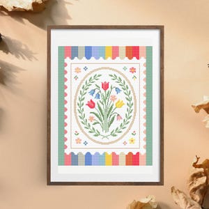 Puede incluir: Una obra de arte en punto de cruz enmarcada con un ramo floral en un marco ovalado. El ramo incluye tulipanes rojos, campanillas azules y flores amarillas. La obra est&aacute; rodeada por un borde a rayas de colores y un borde festoneado.