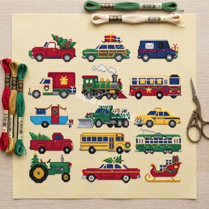 Op de afbeelding: Een kruissteekpatroon op beige Aida-stof met twaalf voertuigen in kerstthema, waaronder vrachtwagens, een trein, een bus, een tractor en een arrenslee. Inclusief groene en beige strengen borduurgaren en een metalen schaar.