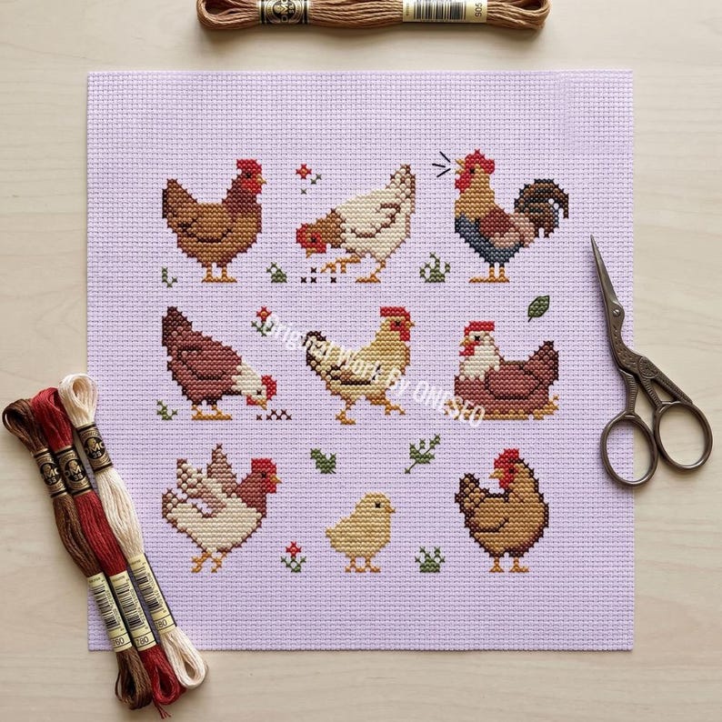 May include: A cross-stitch design featuring various chickens and a rooster in shades of brown, red, and white on a lavender background. Embroidery floss and scissors are also visible. The design includes small floral and leaf accents.