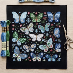 May include: Black needlepoint canvas featuring a colorful butterfly design. The butterflies are in shades of blue, green, and white, with floral and snowflake accents. Embroidery floss and scissors are also visible.