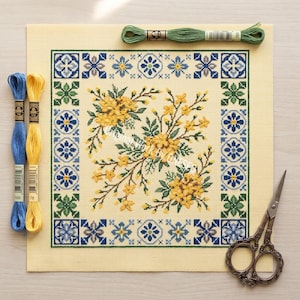 May include: A needlepoint canvas featuring a yellow and green floral design, framed by a blue and green geometric border. Blue and yellow embroidery threads and small scissors are also visible.