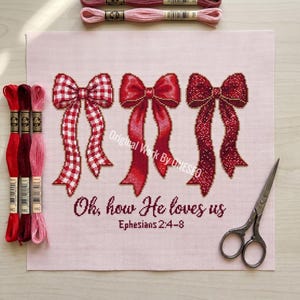 Könnte beinhalten: Ein Kreuzstichprojekt auf hellrosa Stoff mit drei verschiedenen roten Schleifen und dem Text "Oh, how He loves us Ephesians 2:4-8". Das Design wird von drei Stickgarnsträngen in Rot- und Rosatönen sowie einer Metallschere begleitet.