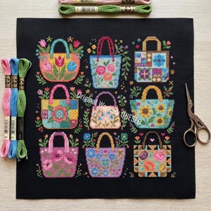 Puede incluir: Un cuadrado de tela negra con un patr&oacute;n de punto de cruz de nueve bolsos coloridos decorados con varios dise&ntilde;os florales y geom&eacute;tricos. Tres madejas de hilo de bordar en rosa, azul y verde, y unas tijeras de metal est&aacute;n colocadas cerca.