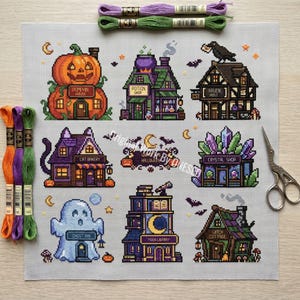 Könnte beinhalten: Ein Kreuzstichmuster auf hellgrauem Stoff mit neun Gebäuden zum Thema Halloween, darunter ein Kürbishaus, ein Zaubertrankladen, ein Rabenhaus, eine Katzenbäckerei, ein Kristallladen, ein Geistergasthaus, eine Mondbibliothek und ein Hexenhäuschen, mit Stickgarn und einer Schere.