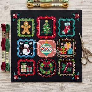May include: A black fabric square featuring nine embroidered Christmas-themed squares, including a gingerbread man, tree, stocking, snowman, ornament, gifts, wreath, and candy cane. Two embroidery floss skeins and metal scissors are included.