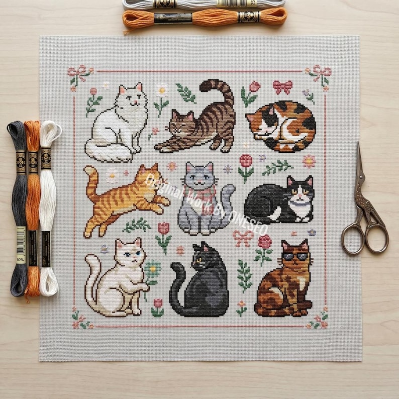 May include: A cross-stitch pattern featuring nine different cat designs in various poses and colors, surrounded by floral and bow accents. Embroidery floss and scissors are also visible, suggesting a crafting project.