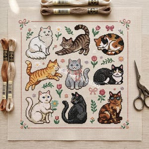 May include: A cross-stitch design showcasing nine cat illustrations in diverse colours and poses, framed by floral and bow patterns. Embroidery threads and scissors are present, indicating a crafting project.