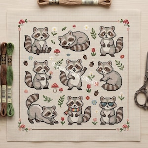 May include: Cross-stitch pattern featuring nine cartoon raccoons in various poses, surrounded by floral and mushroom motifs. The raccoons have gray and brown fur with striped tails. The design is on a beige fabric, with embroidery floss and scissors in the background.