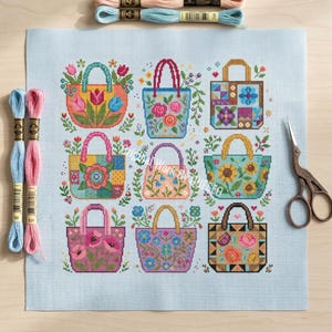 Puede incluir: Un patr&oacute;n de punto de cruz sobre tela azul claro que presenta nueve bolsos distintos decorados con varios motivos florales, patrones geom&eacute;tricos y dise&ntilde;os coloridos. El conjunto incluye dos madejas de hilo y tijeras de metal.