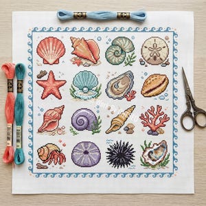 May include: A square cross-stitch pattern on white fabric featuring a grid of sixteen marine life illustrations including various seashells, a starfish, a sand dollar, coral, and a sea urchin, framed by a blue wave border with embroidery floss and scissors.
